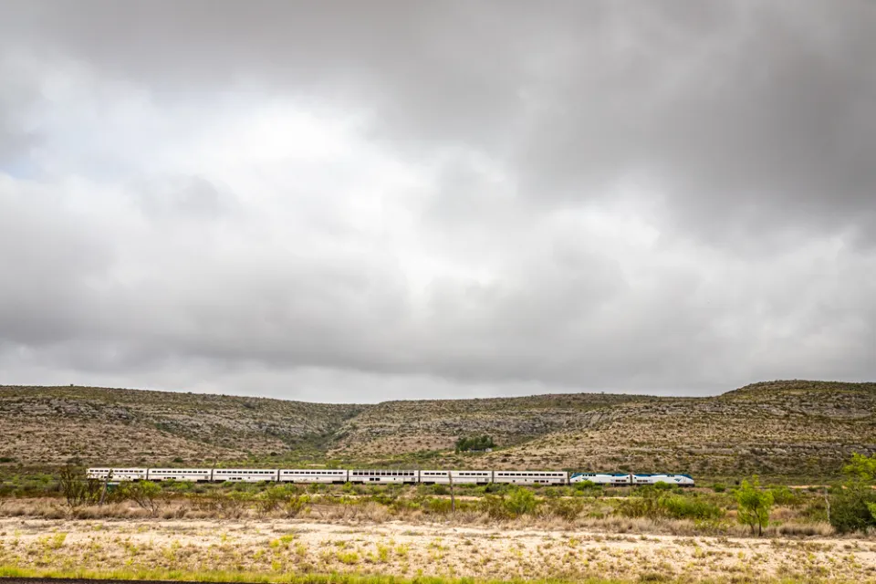 Amtrak Sunset Limited train viewed from the side passing low desert hills in West Texas